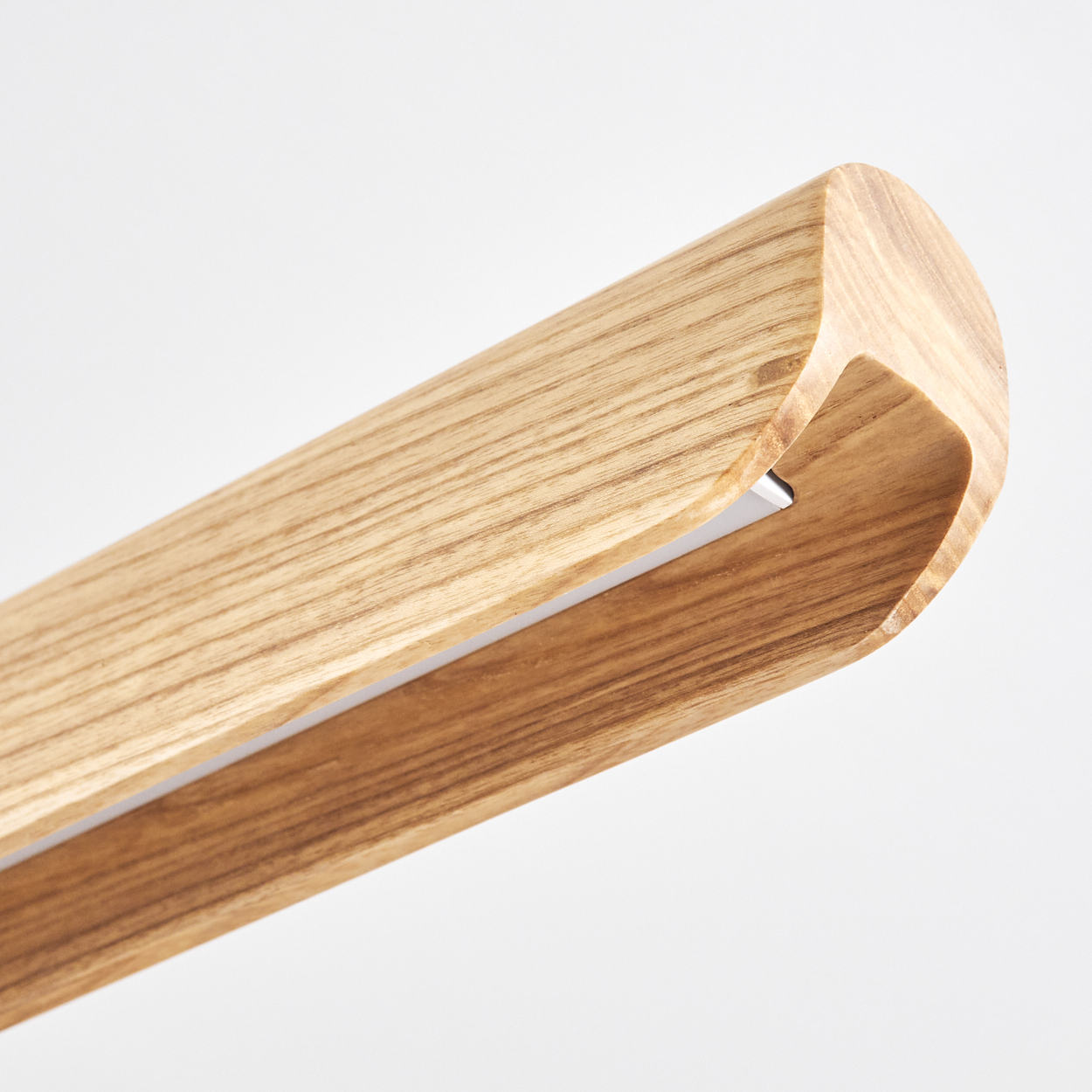 Nahaufnahme eines Holzbalkens mit abgerundeten Kanten. Er ist hellbraun mit Holzmaserung. Ein Metallstreifen ist in der Nut sichtbar.