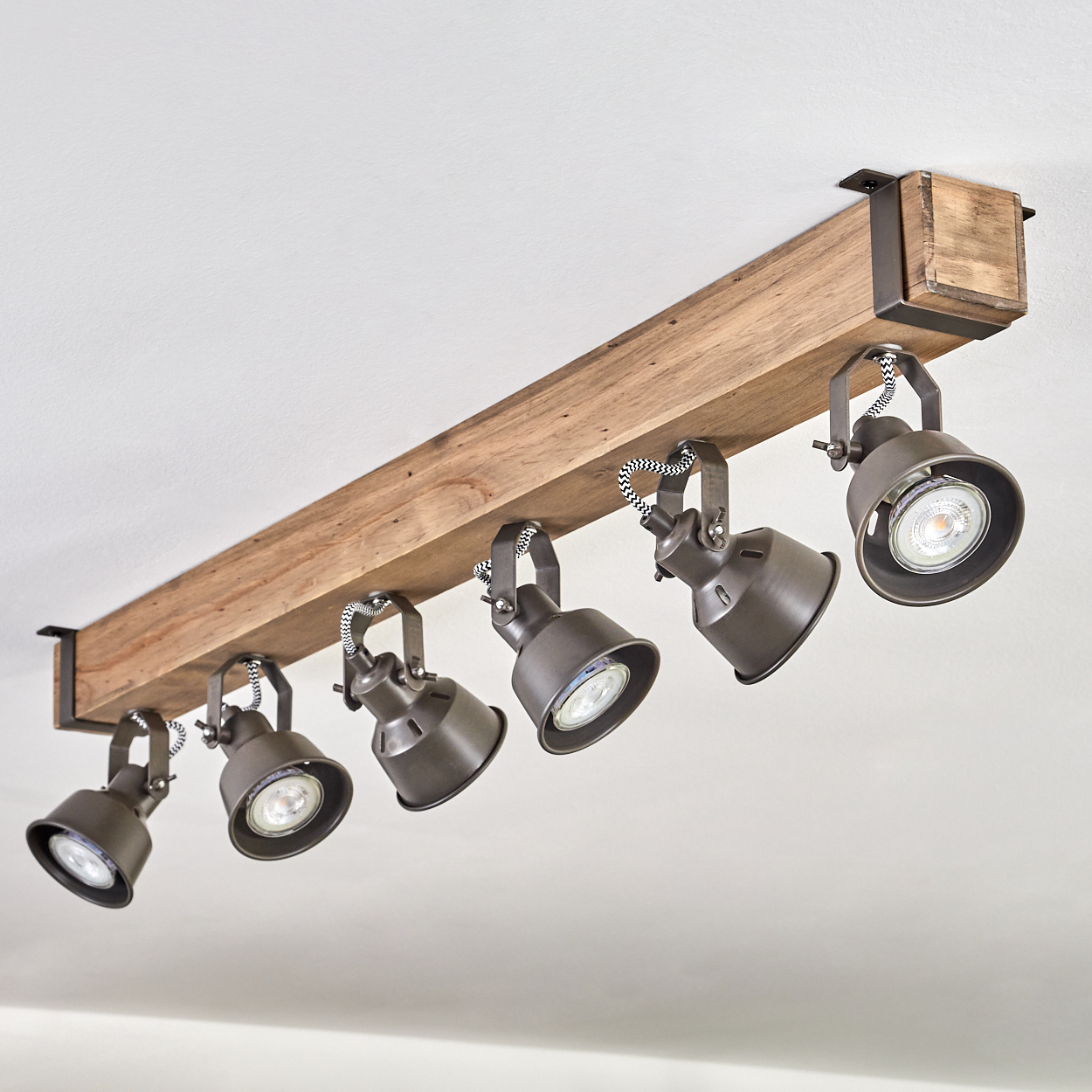 Ein Holzbalken mit sechs daran befestigten Strahlern. Die Lichter sind nach unten gerichtet, der Hintergrund ist die Decke.