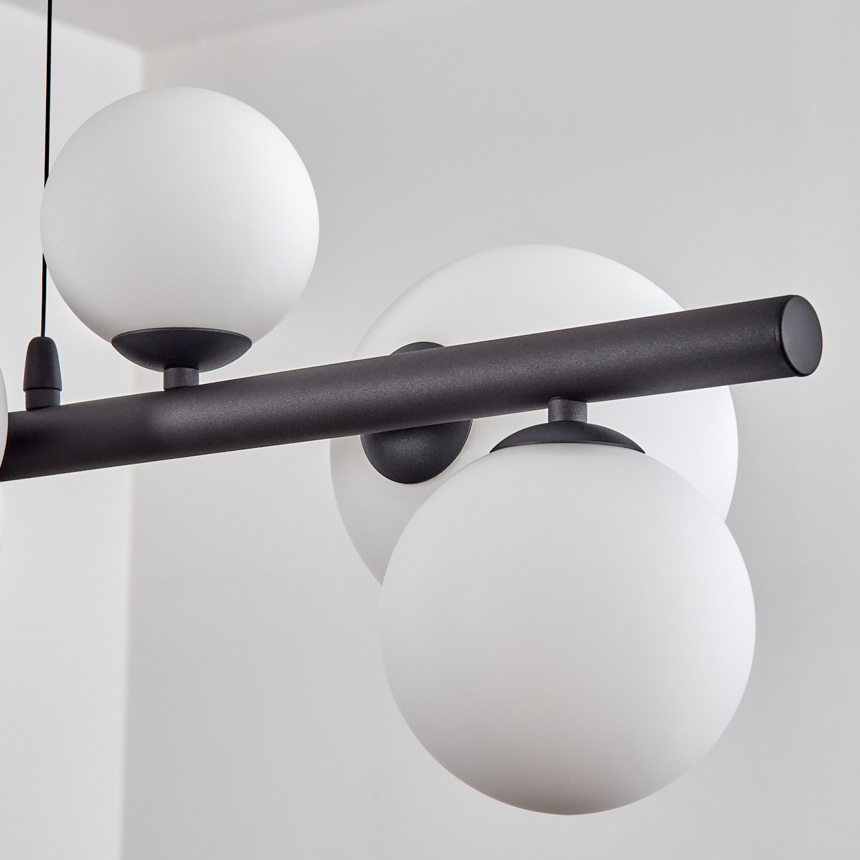 Eine moderne schwarze Pendelleuchte mit mehreren weißen, kugelförmigen Lichtern hängt vor einer weißen Wand.