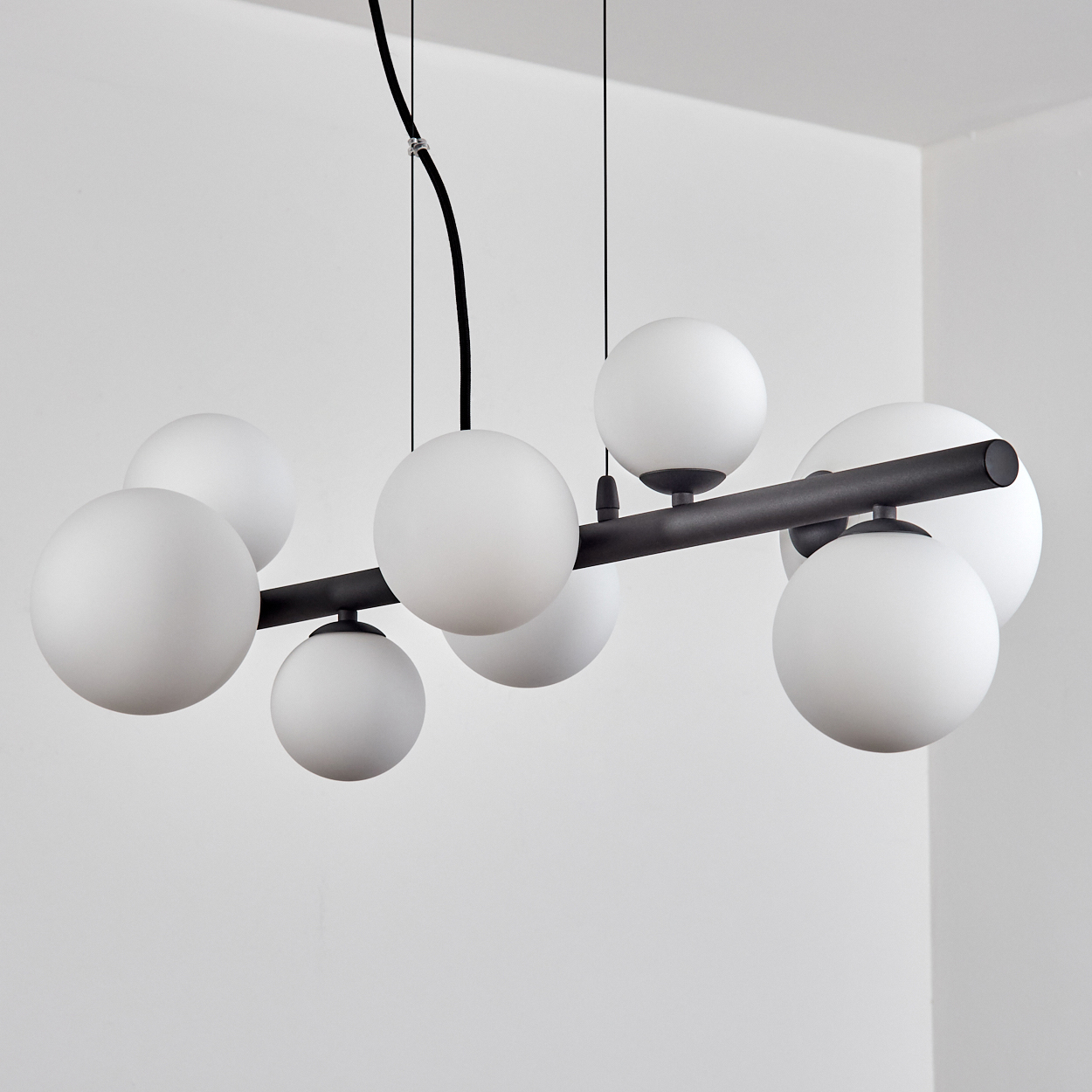 Eine moderne Deckenleuchte mit weißen Kugeln und einer dunklen Metallstange, vor weißer Wand.