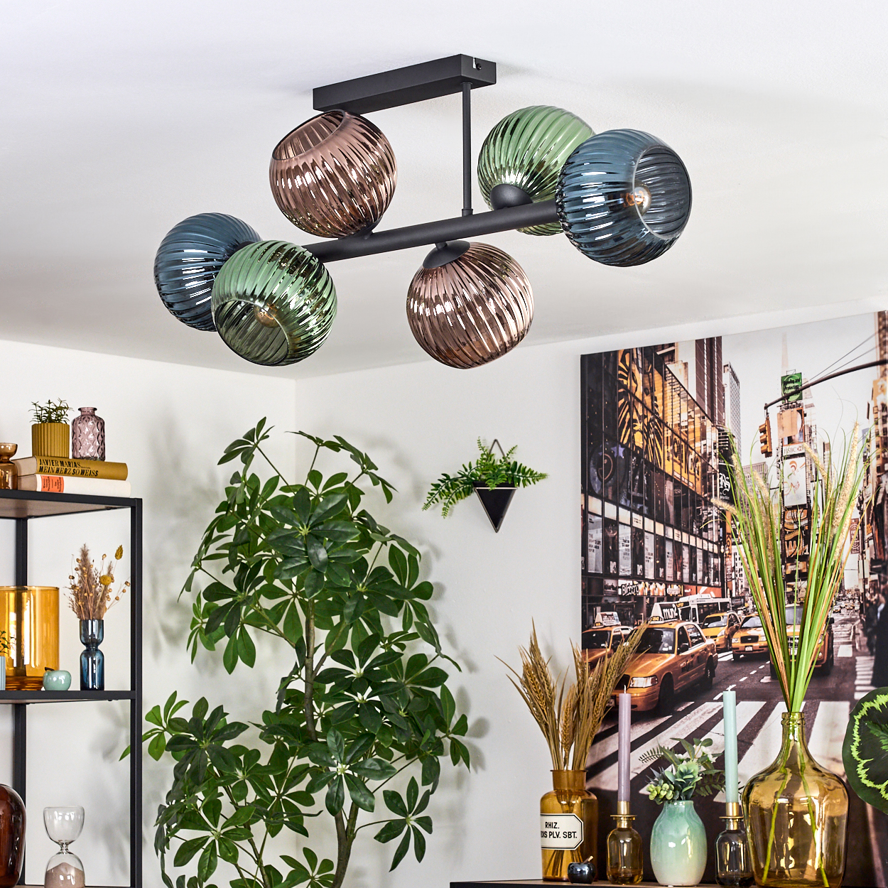 Eine moderne Deckenlampe mit Glaskugeln, eine große Pflanze und ein Stadtbildgemälde im Hintergrund.