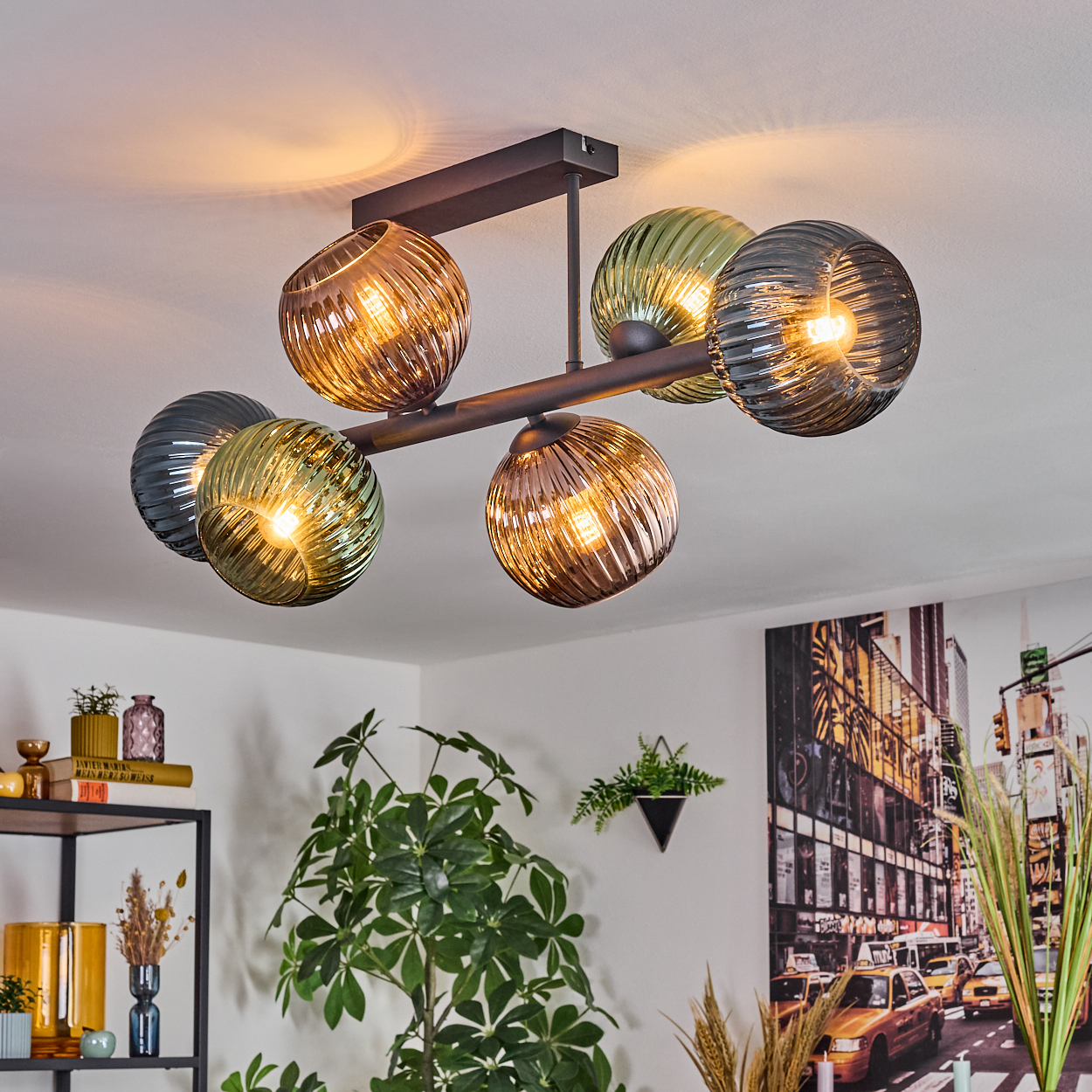 Eine moderne Deckenleuchte mit sechs kugelförmigen Lichtern in verschiedenen Farben, die an einem dunklen Metallrahmen hängen. Im Hintergrund ist ein Raum.