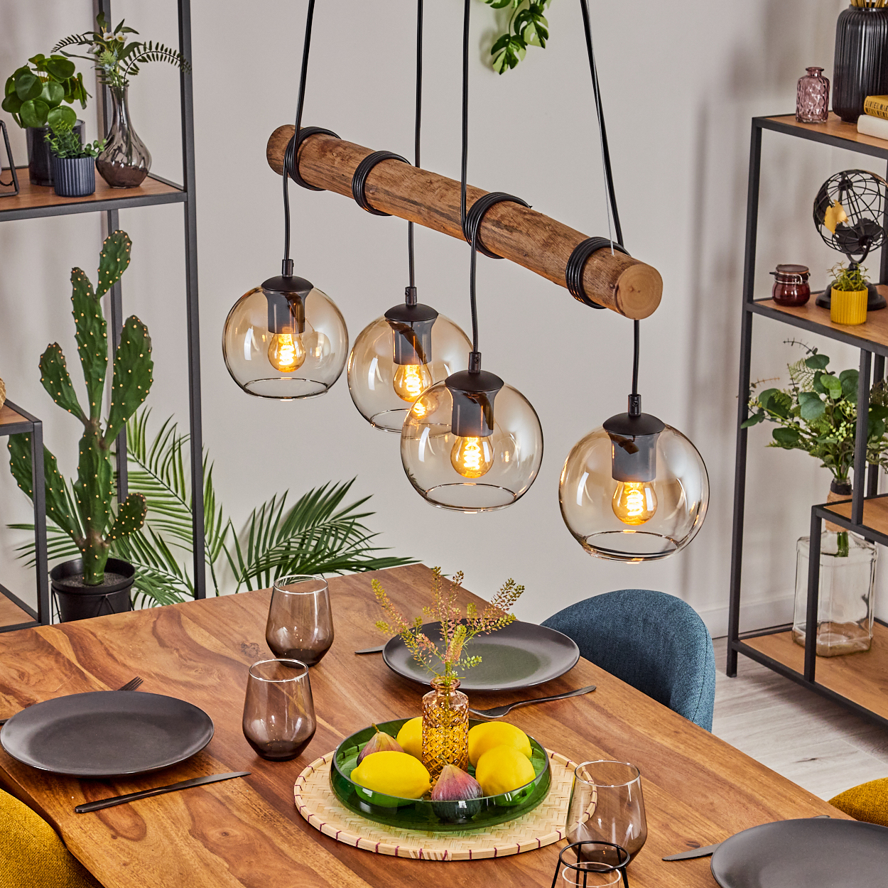Esszimmer mit Holztisch, Hängelampen und Tischgedeck. Im Hintergrund stehen Pflanzen auf Regalen.