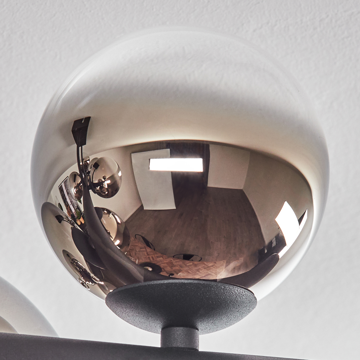 Nahaufnahme einer dekorativen Leuchte mit einer großen, reflektierenden Kugel. Die Kugel spiegelt den Raum mit Holzboden wider.