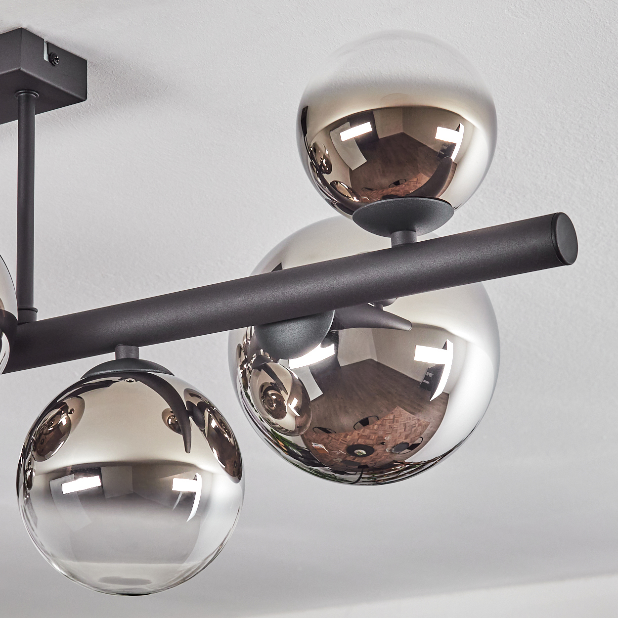 Eine moderne Deckenleuchte mit vier reflektierenden, kugelförmigen Glasschirmen. Die Leuchte ist schwarz und an einer weißen Decke befestigt.