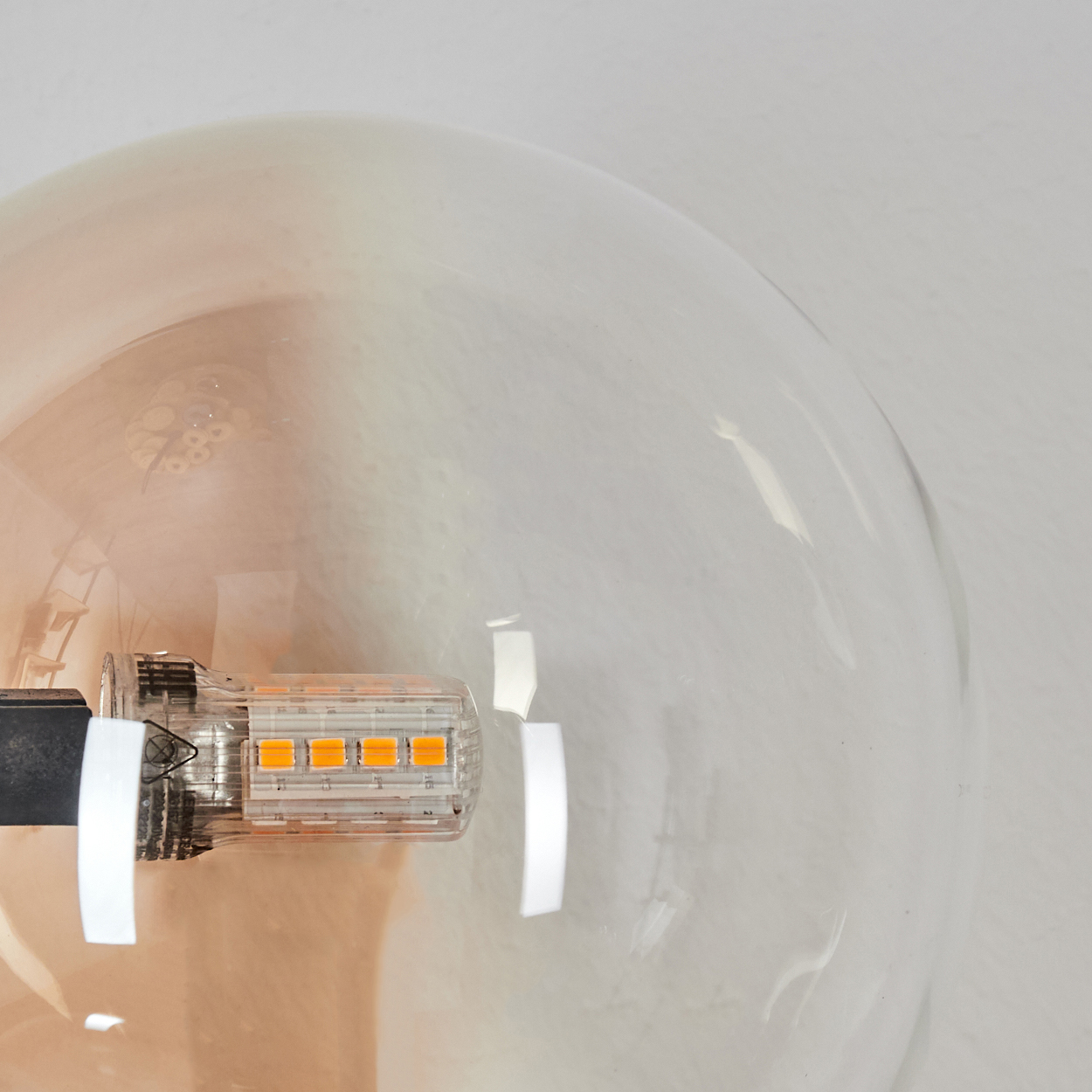 Nahaufnahme einer klaren Glühbirne. Im Inneren ist ein orangefarbenes LED-Licht sichtbar. Die Glühbirne ist vor einem weißen Hintergrund.