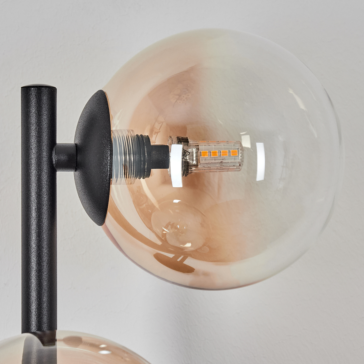 Nahaufnahme einer modernen Lampe. Ein schwarzer Metallrahmen trägt einen Glaskolben mit einer orangefarbenen Glühbirne. Der Hintergrund ist weiß.