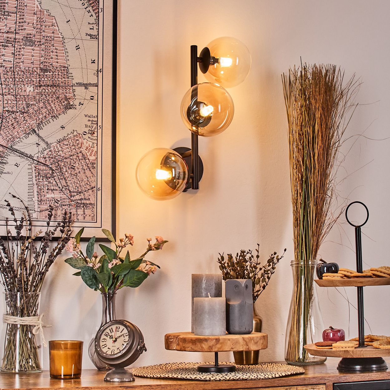 Innenaufnahme mit Karte, Wandlampe, Blumen, Kerzen und Dekorationsartikeln auf einer Holzoberfläche.
