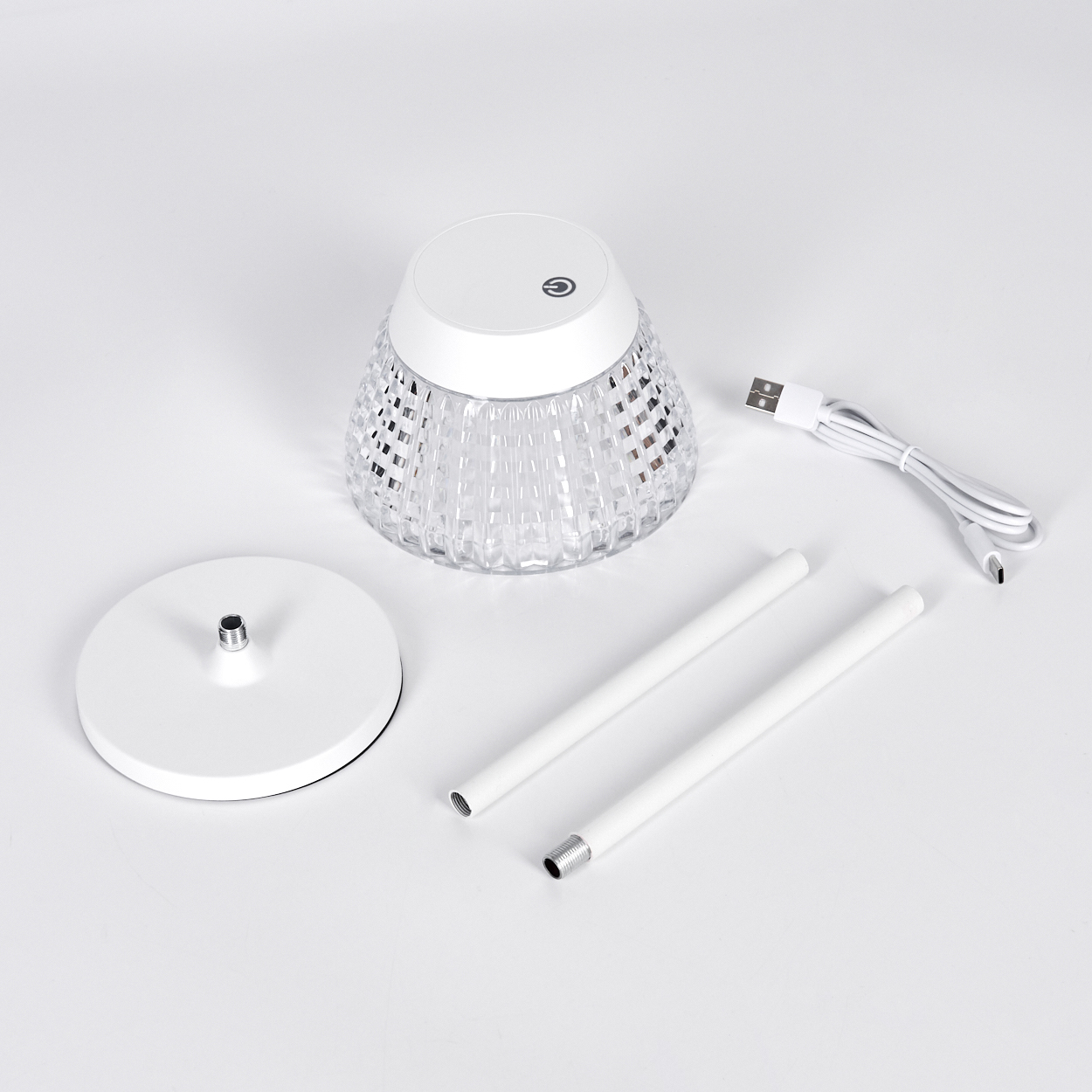 Eine zerlegte weiße Tischlampe mit Kristallschirm, Sockel, zwei Stangen und einem USB-Ladekabel auf weißem Untergrund.
