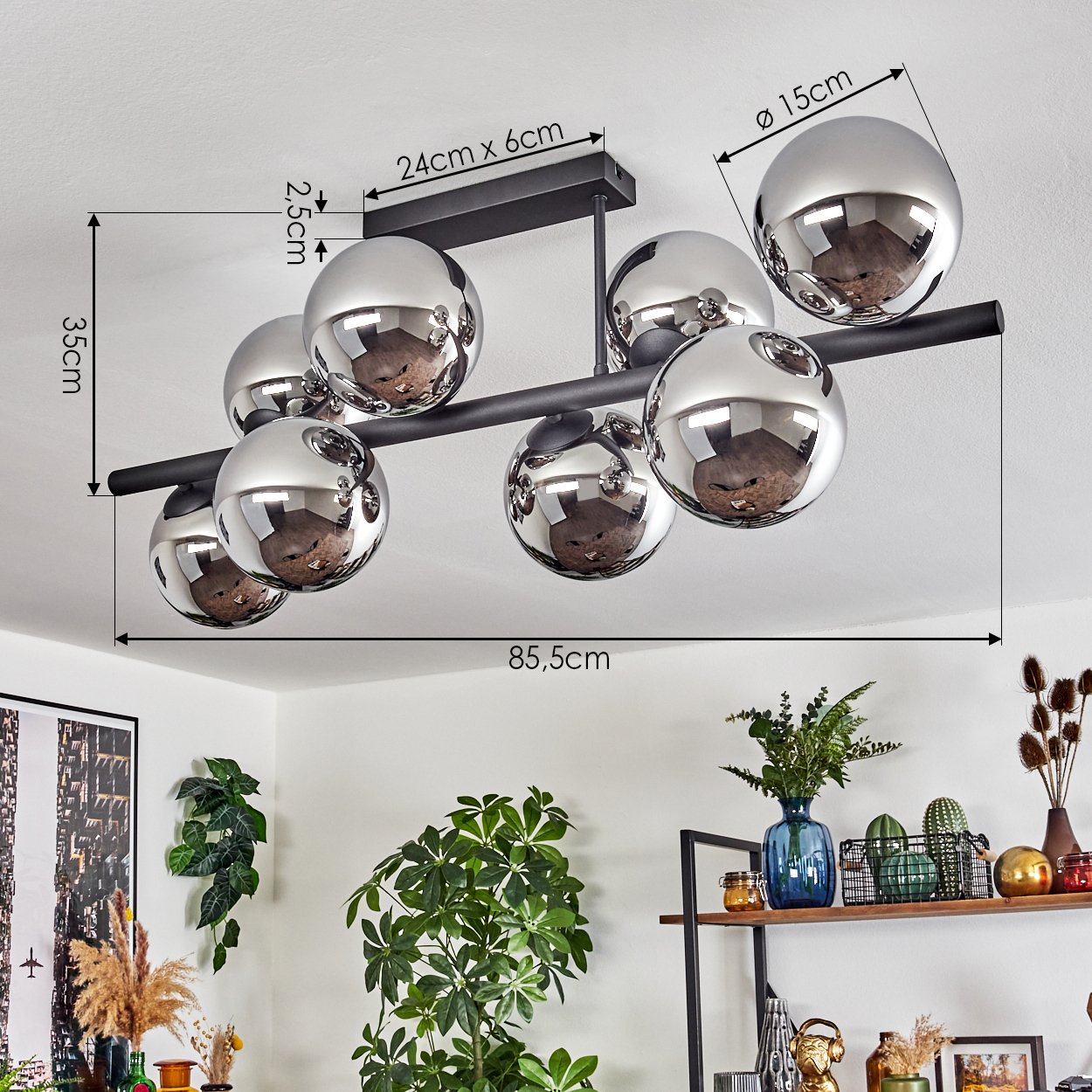 Eine moderne Deckenlampe mit silbernen Kugeln. Die Abmessungen der Lampe sind beschriftet. Pflanzen und ein Regal mit Dekorationen im Hintergrund.