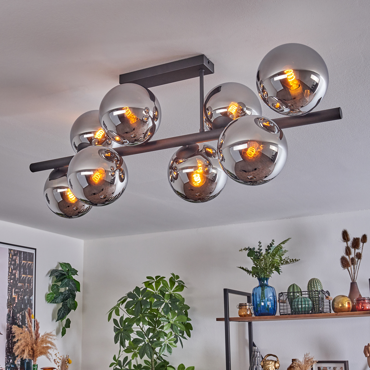 Moderne Deckenlampe mit acht Chromkugeln, die den Raum reflektieren. Pflanzen und ein Regal im Hintergrund.