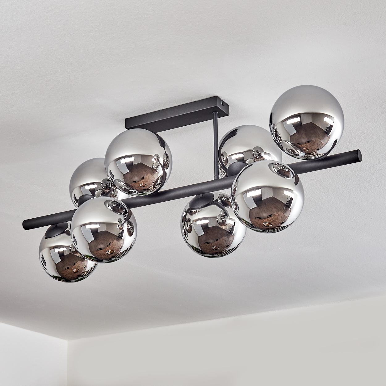 Eine moderne Deckenleuchte mit acht verchromten Kugeln, die an einem schwarzen Metallrahmen hängen und den Raum reflektieren.