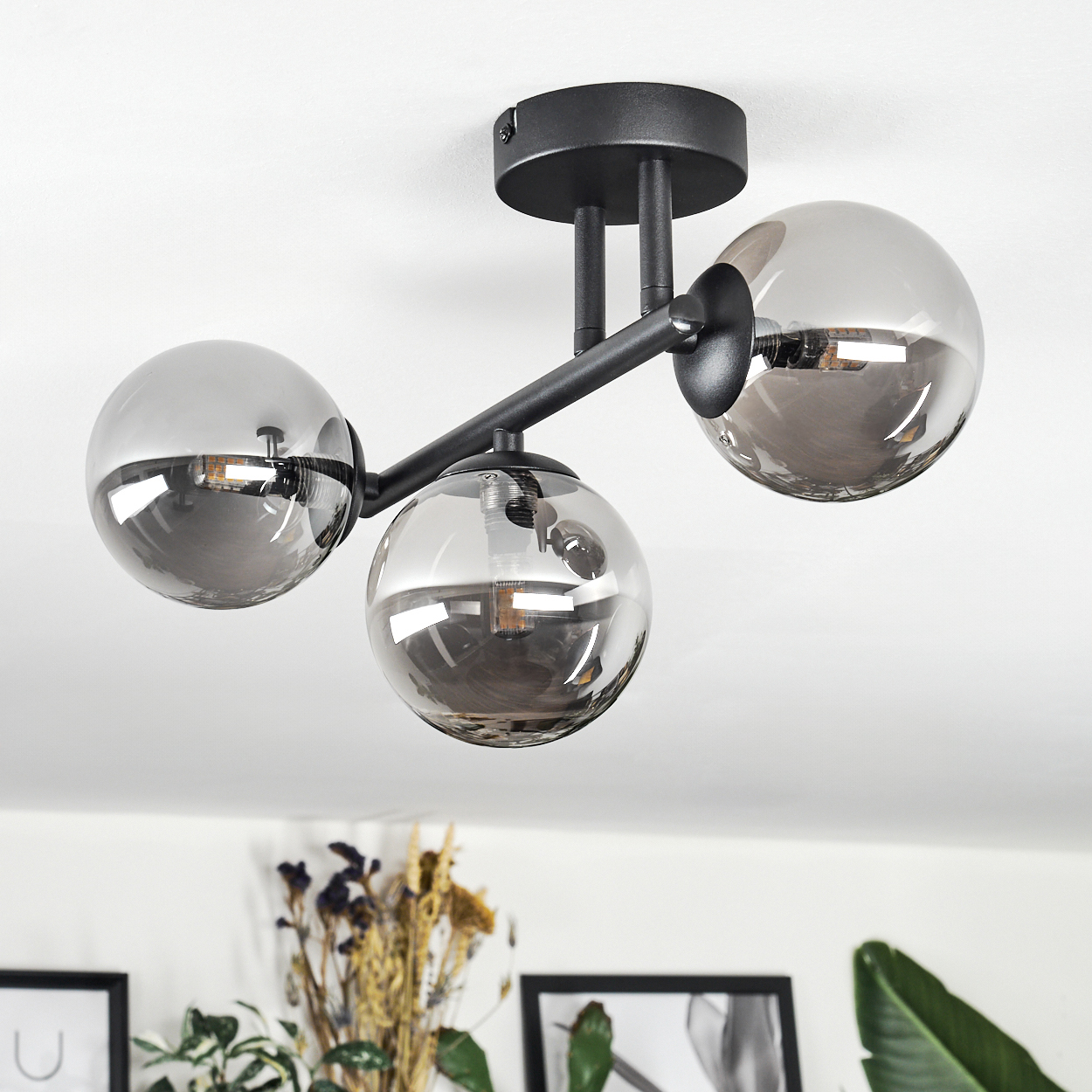 Eine moderne Deckenlampe mit drei kugelförmigen Schirmen. Die Schirme sind grau und reflektieren den Raum. Die Lampe ist schwarz.