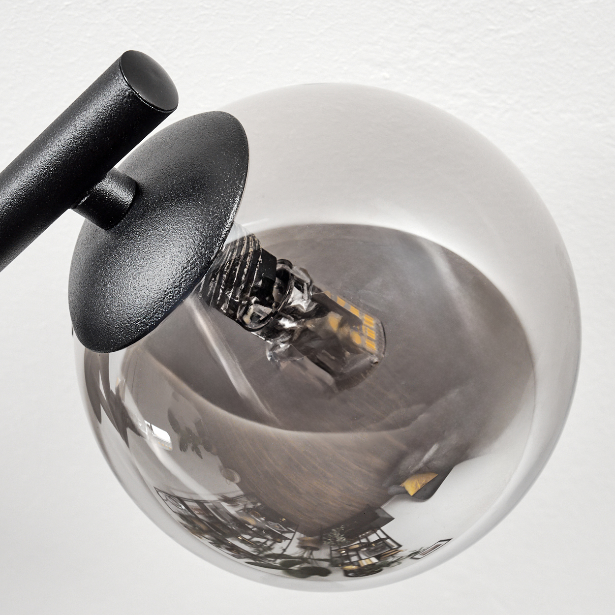 Nahaufnahme einer schwarzen Lampe mit runder Glaskugel. Die Kugel reflektiert einen Raum. Die Lampe ist vor einer weißen Wand.