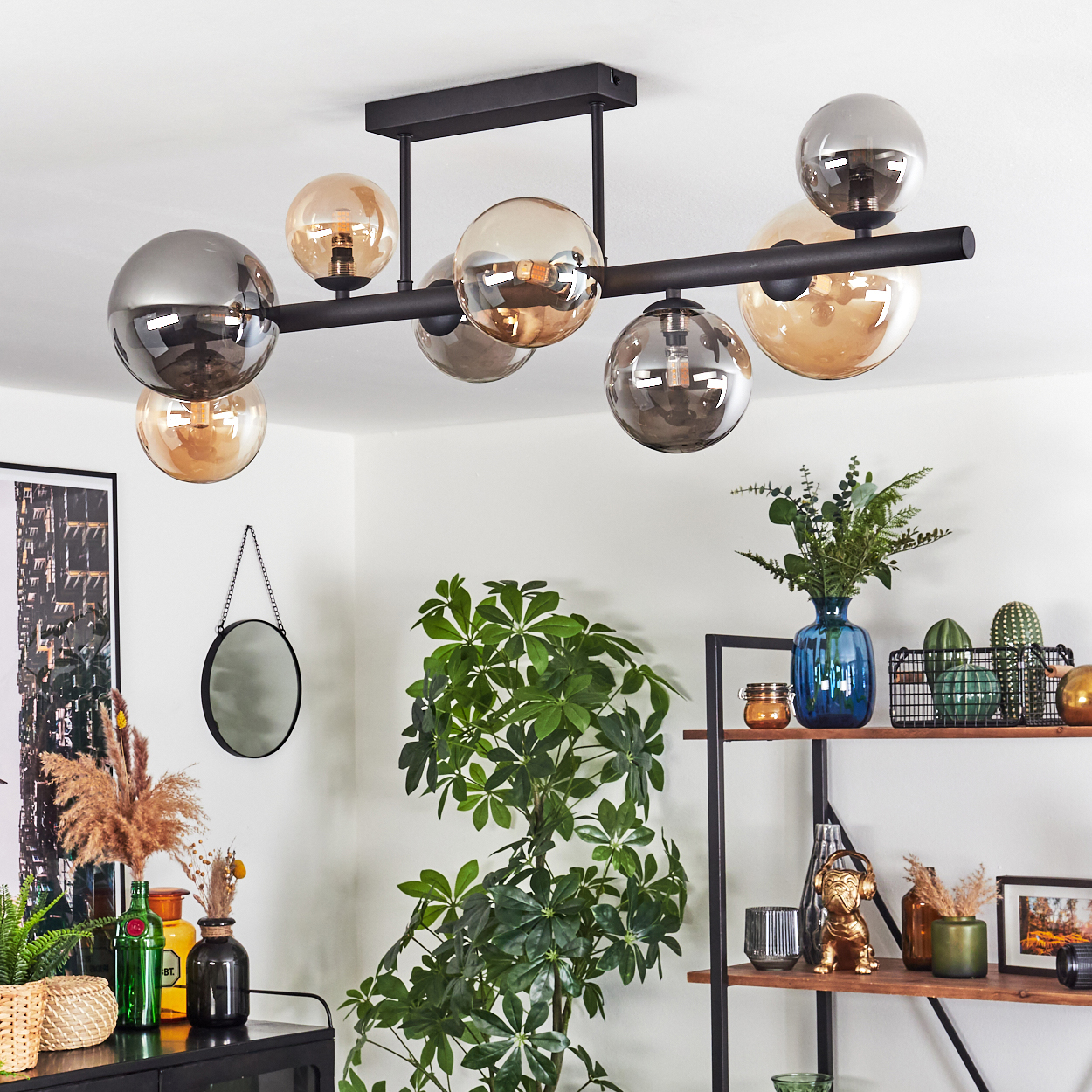 Modernes Wohnzimmer mit schwarzem Kronleuchter, Pflanzen und Regalen mit Dekorationen. Der Kronleuchter hat Glaskugeln.