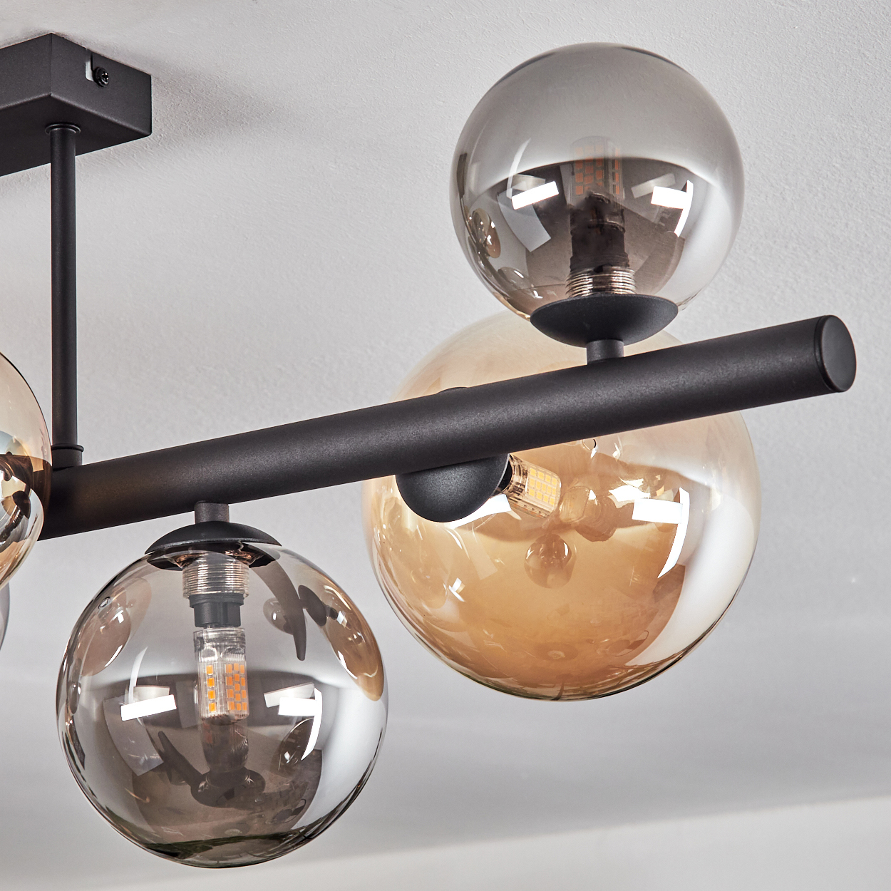 Eine moderne schwarze Deckenleuchte mit mehreren Glaskugelschirmen in Grau- und Bernsteintönen, mit sichtbaren Glühbirnen.