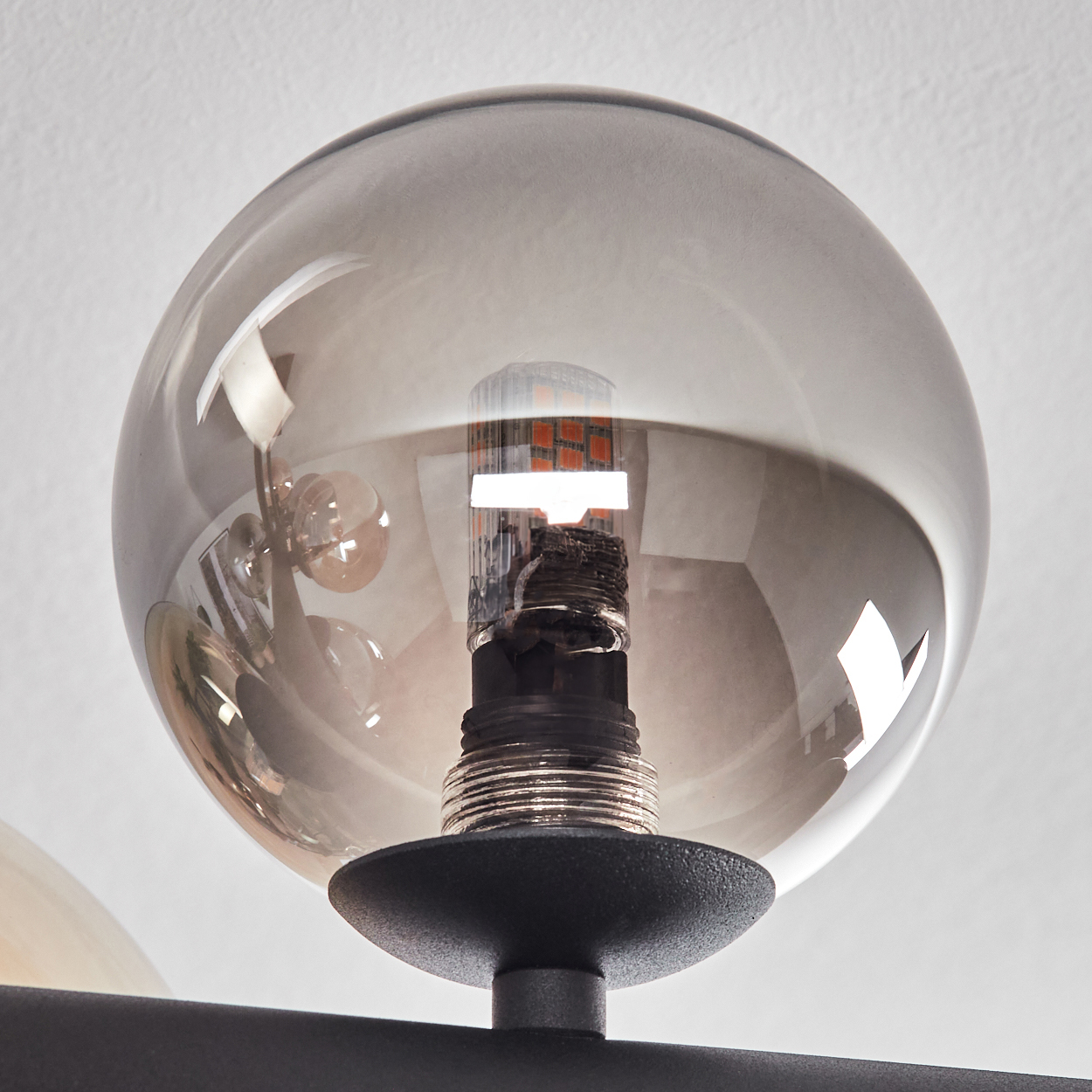 Nahaufnahme einer Leuchte, die einen kugelförmigen, rauchfarbenen Glasschirm um eine Glühbirne zeigt. Die Leuchte ist schwarz.