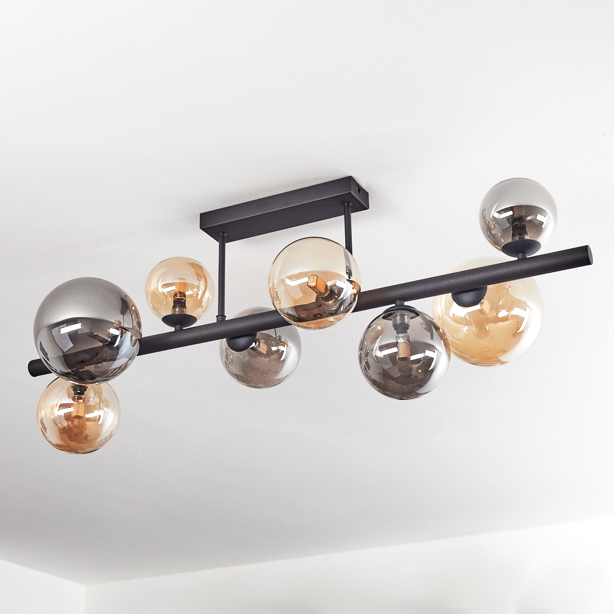 Eine moderne Deckenleuchte mit mehreren Glaskugelschirmen in Bernstein und Silber. Schwarze Metallstangen und eine weiße Decke.