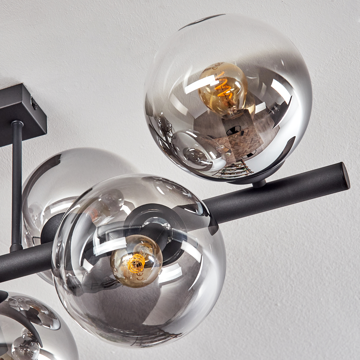 Eine moderne Deckenleuchte mit mehreren kugelförmigen Glasschirmen, in denen sich jeweils eine warm getönte Glühbirne befindet, vor einer weißen Wand.