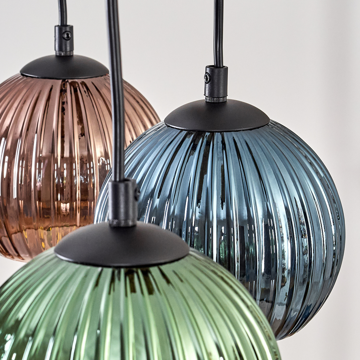 Drei farbige Glashängelampen: Bronze, Blau und Grün. Sie haben schwarze Armaturen und hängen vor einem weißen Hintergrund.