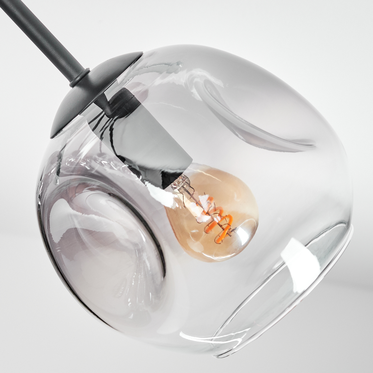 Nahaufnahme einer Glas-Pendelleuchte. Die Leuchte hat einen klaren, bauchigen Schirm mit einer sichtbaren Glühbirne. Das Gestell ist schwarz.