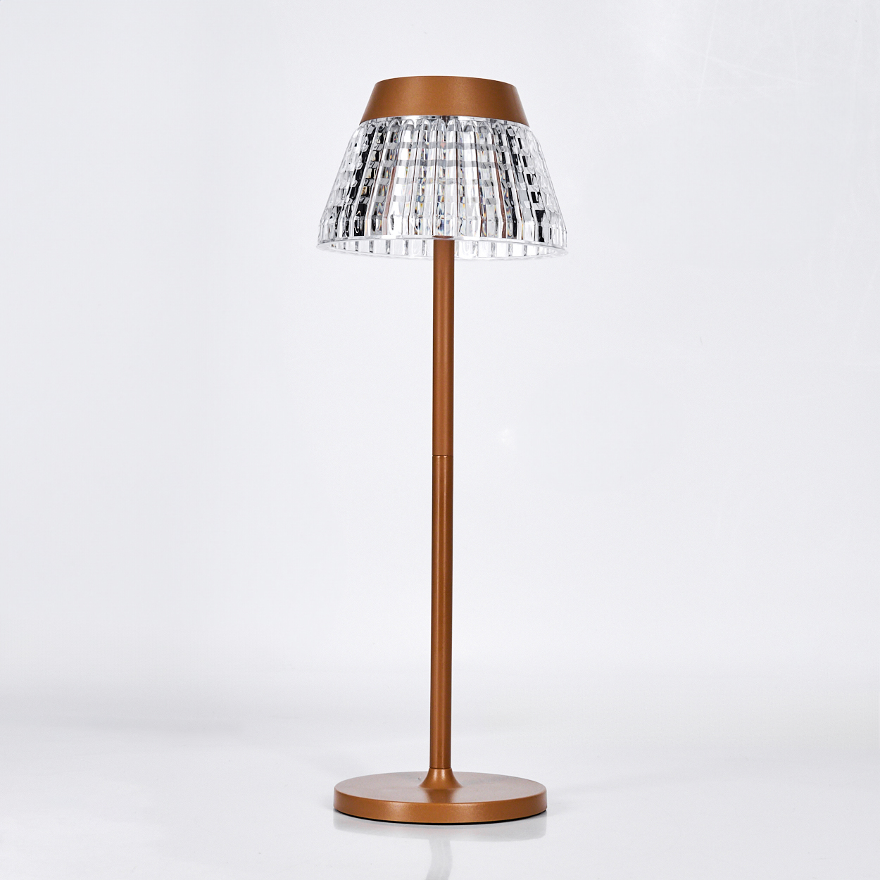 Eine moderne Tischlampe mit bronzefarbenem Fuß und Stiel sowie einem durchsichtigen, facettierten Lampenschirm. Der Hintergrund ist weiß.