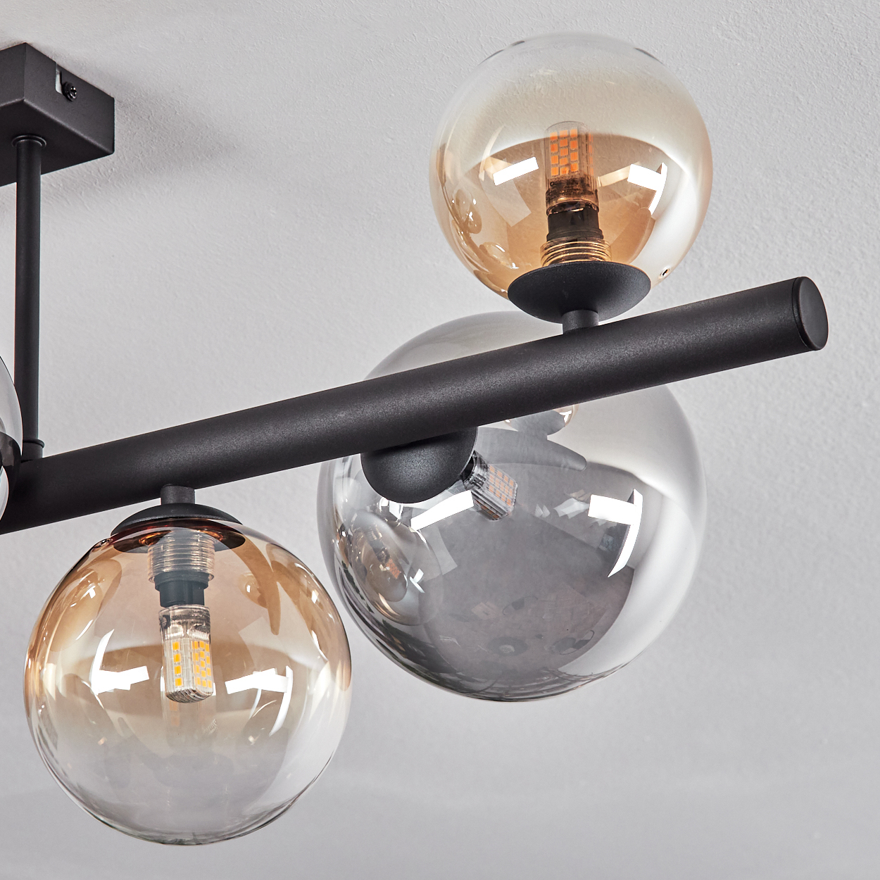 Eine moderne Deckenleuchte mit schwarzen Metallstangen und kugelförmigen Glasschirmen. Einige Schirme sind bernsteinfarben, andere klar.