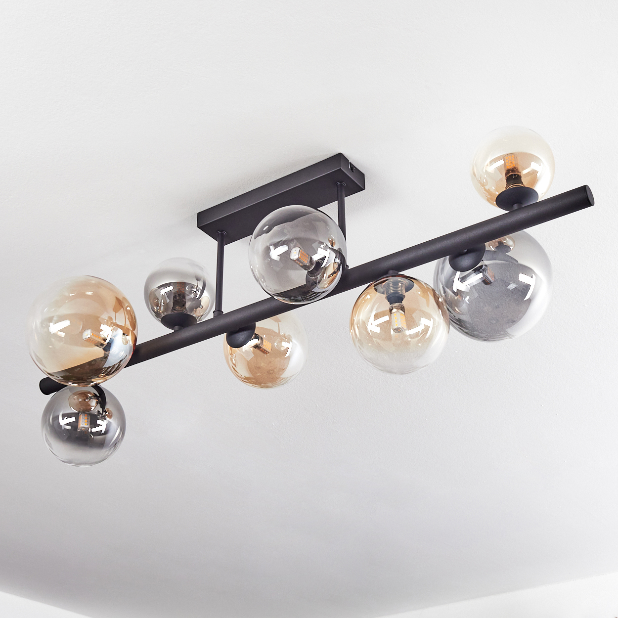 Eine moderne schwarze Pendelleuchte mit acht kugelförmigen Glasschirmen in Bernstein und Silber, vor einer weißen Decke.
