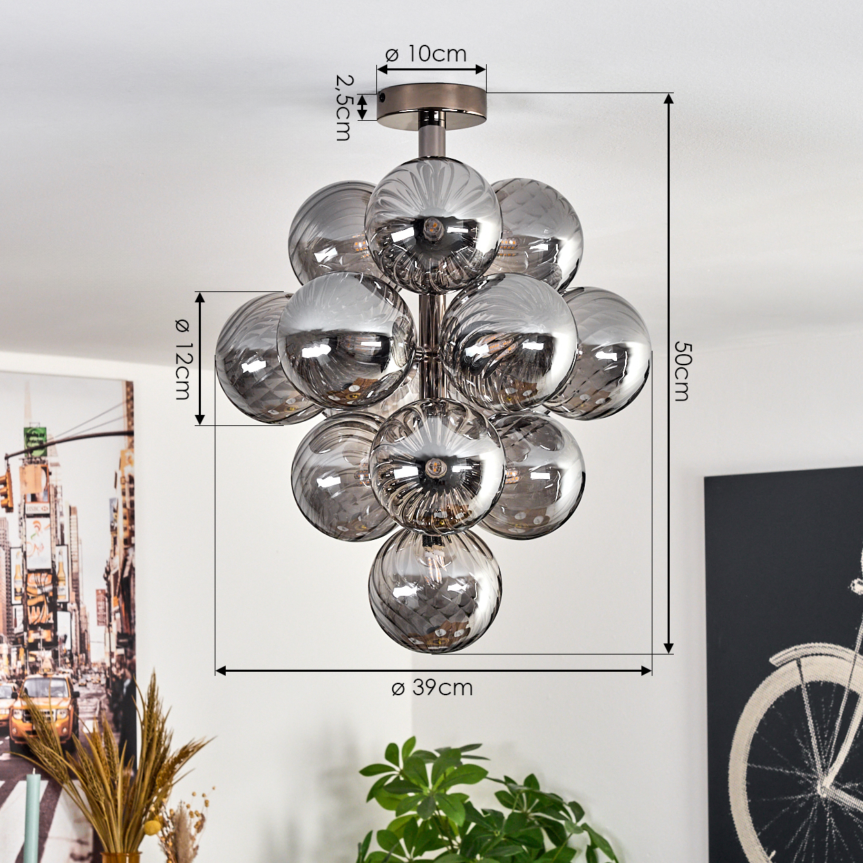 Eine moderne silberne Deckenleuchte mit mehreren Glaskugeln hängt von einer weißen Decke. Abmessungen sind angegeben.