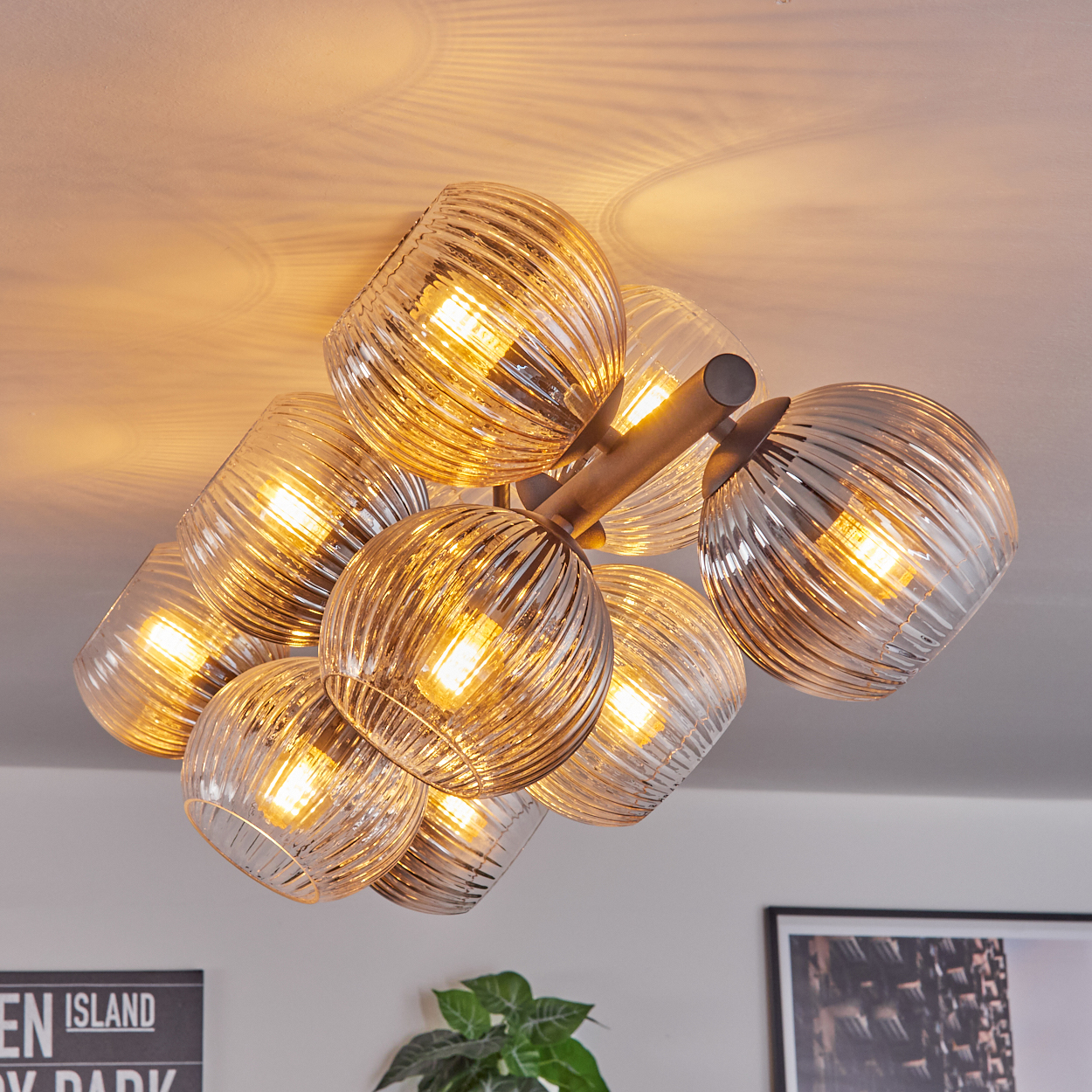 Moderne Deckenleuchte mit mehreren Glaskugelschirmen, die warmes Licht ausstrahlen. Die Leuchte ist an einer weißen Decke befestigt.