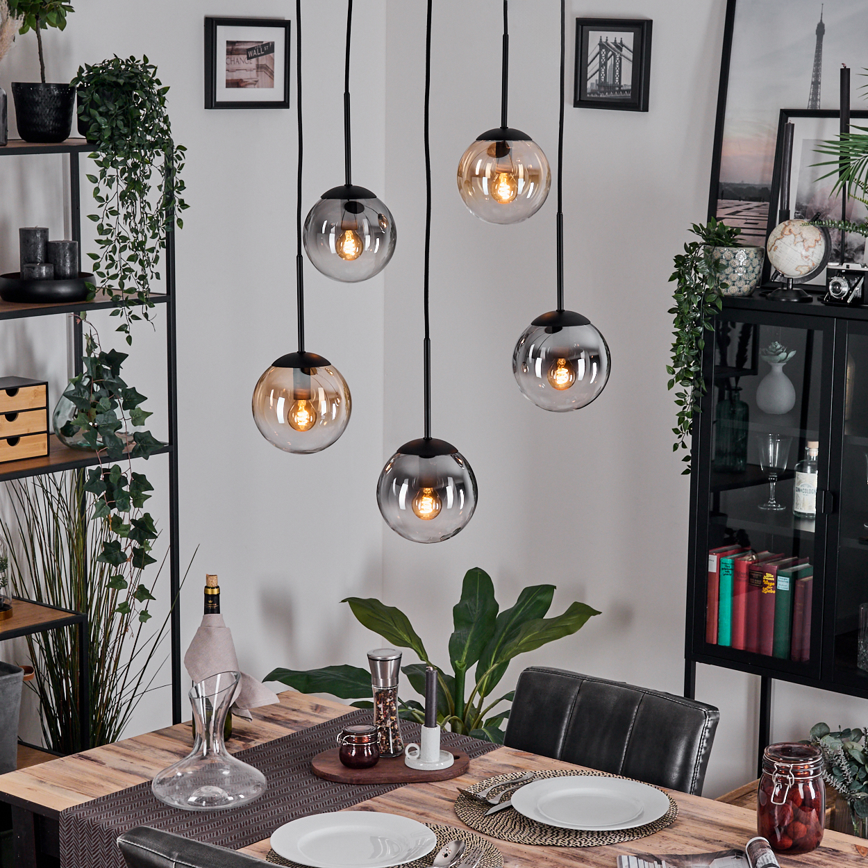 Esszimmer mit Holztisch für Mahlzeit, Hängelampen. Regale mit Deko und Pflanzen. Glasbehälter mit Essen.
