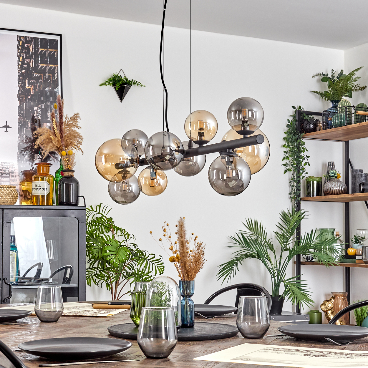 Esszimmer mit Holztisch. Ein Kronleuchter hängt darüber. Pflanzen und Dekoration befinden sich auf Regalen und an den Wänden.