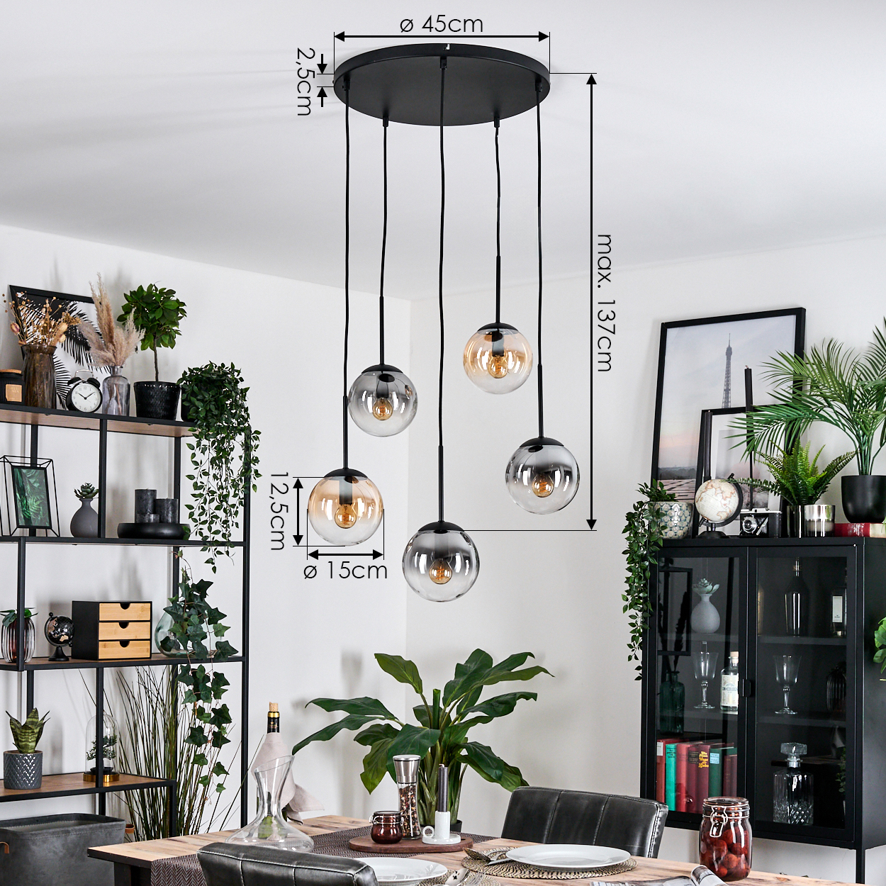 Ein modernes Esszimmer mit einem schwarzen Kronleuchter mit fünf Glaskugeln, Pflanzen und einem Esstisch.