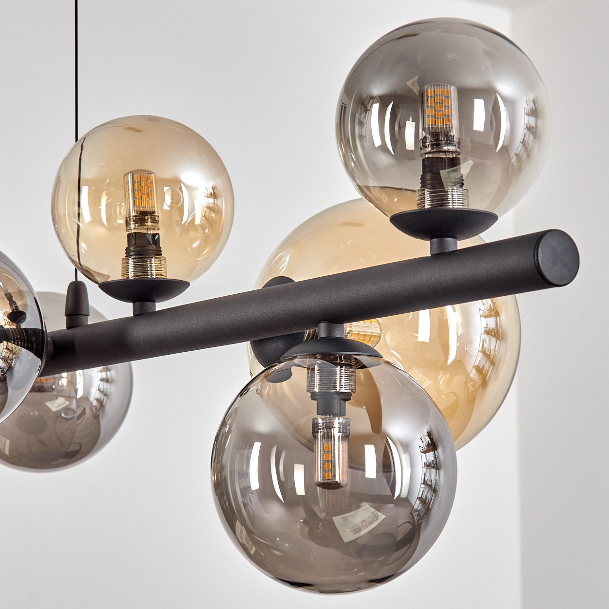 Nahaufnahme einer modernen Deckenleuchte mit kugelförmigen Glasschirmen in Bernstein und Grau. Schwarze Metallbefestigung. Weißer Hintergrund.