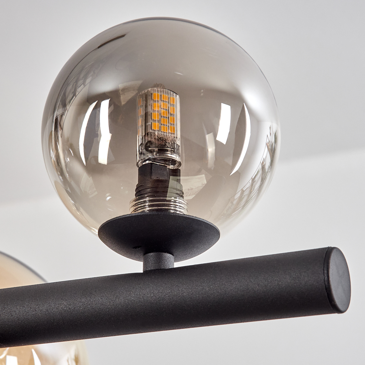 Nahaufnahme eines modernen Kronleuchters. Eine rauchfarbene Glaskugel umgibt eine helle LED-Glühbirne. Schwarze Metallstange und Halterung sind sichtbar.