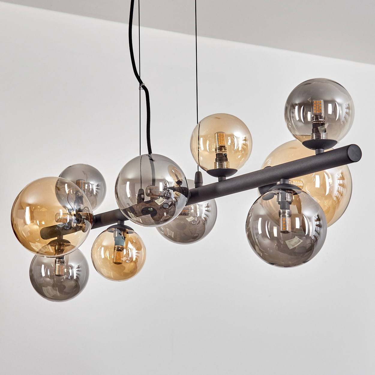 Eine moderne Deckenleuchte mit mehreren kugelförmigen Glasschirmen in Bernstein und Grau, befestigt an einem schwarzen Metallrahmen, vor einer weißen Wand.
