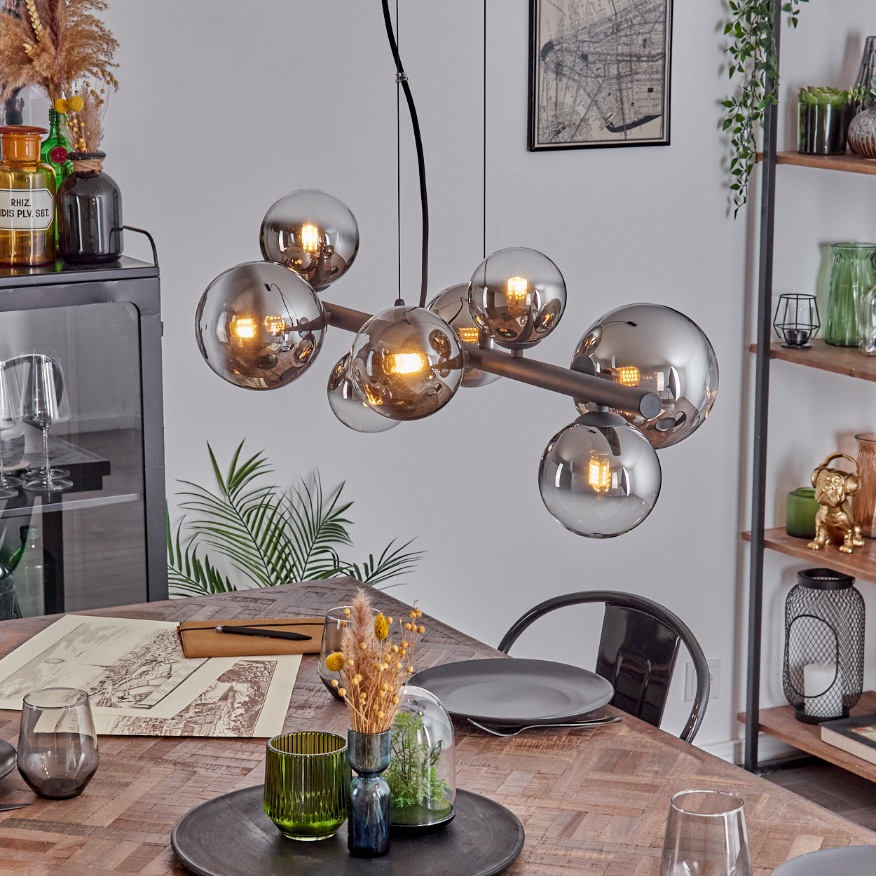 Esszimmer mit Holztisch, moderner Leuchter mit Kugeln und verschiedenen Dekorationen. Ein schwarzer Stuhl ist sichtbar.