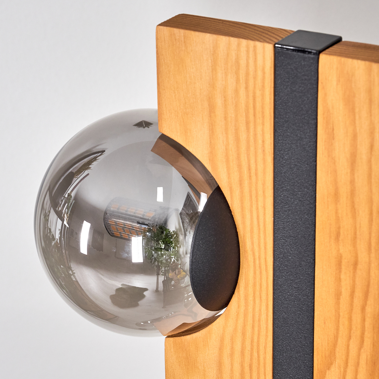 Eine moderne Lampe mit einem rauchfarbenen Glaskugel. Die Lampe ist auf einem Holzsockel mit einem schwarzen Metallstreifen montiert.