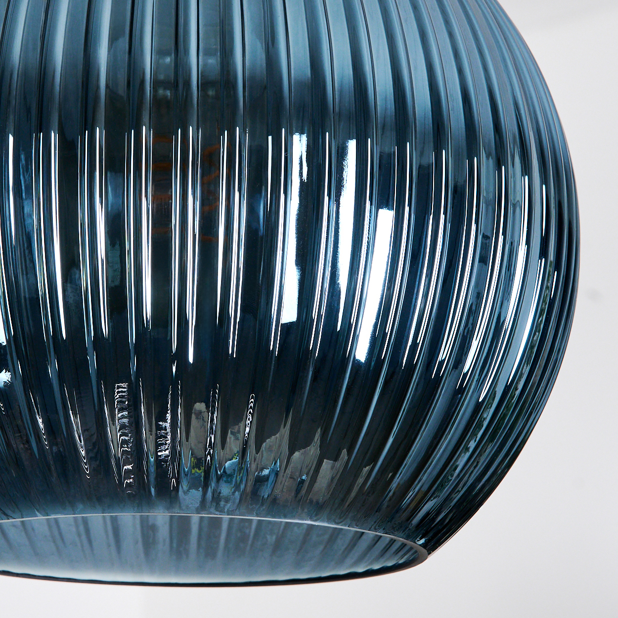 Nahaufnahme eines blauen Glasobjekts mit vertikalen Rippen. Das Glas reflektiert Licht und erzeugt helle Streifen. Der Hintergrund ist weiß.