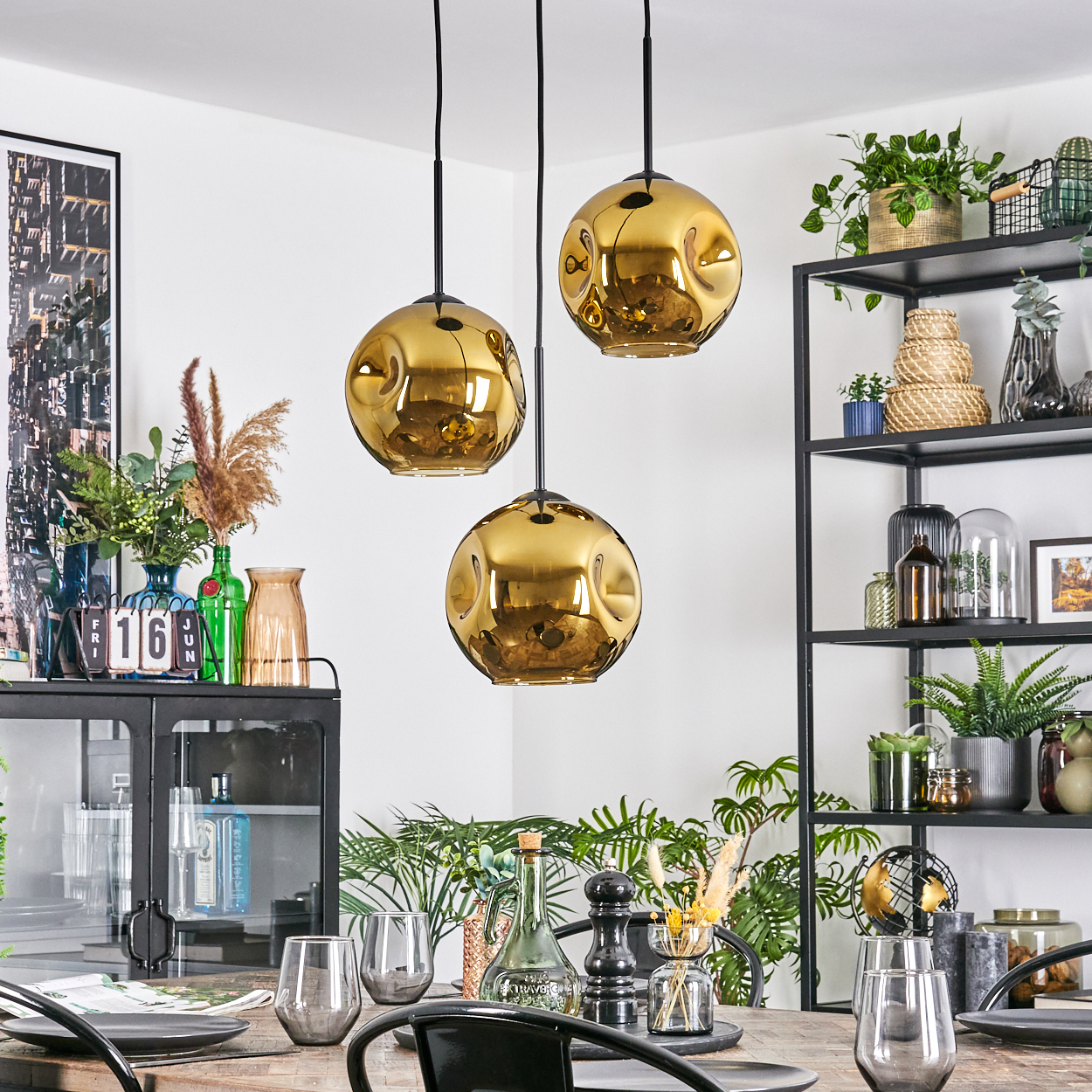 Esszimmer mit goldenen Pendelleuchten, schwarzen Regalen mit Pflanzen, Tisch zum Essen gedeckt.