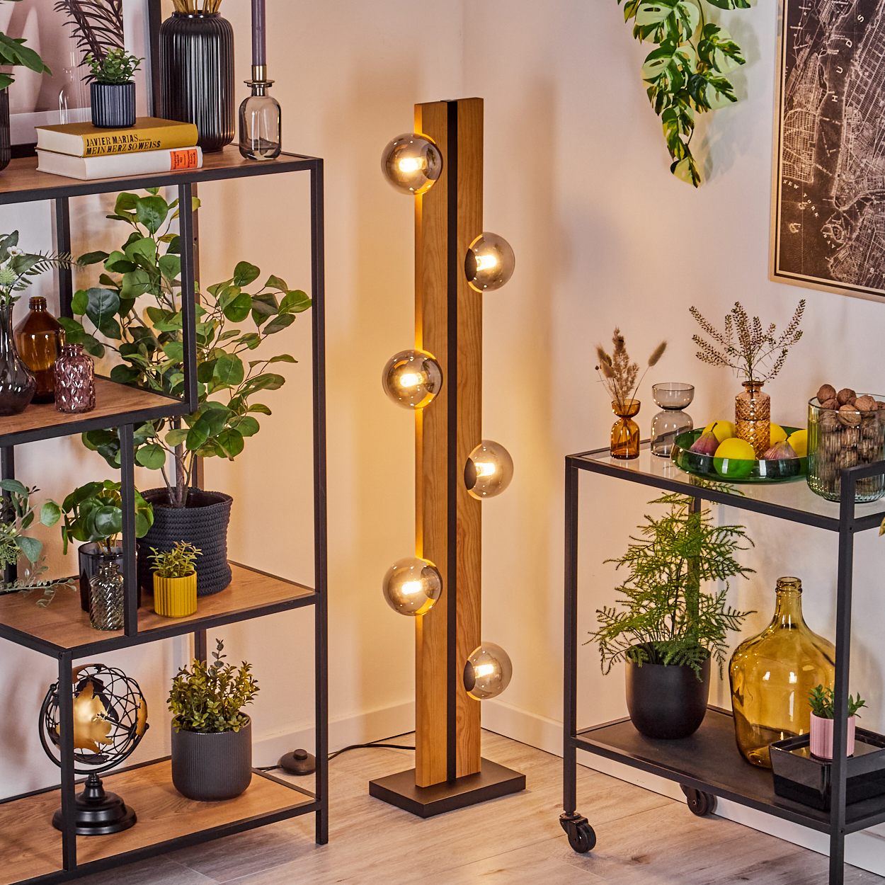 Ein modernes Wohnzimmer mit einer hölzernen Stehlampe, Regalen mit Pflanzen und einem Rollwagen mit Dekoration.