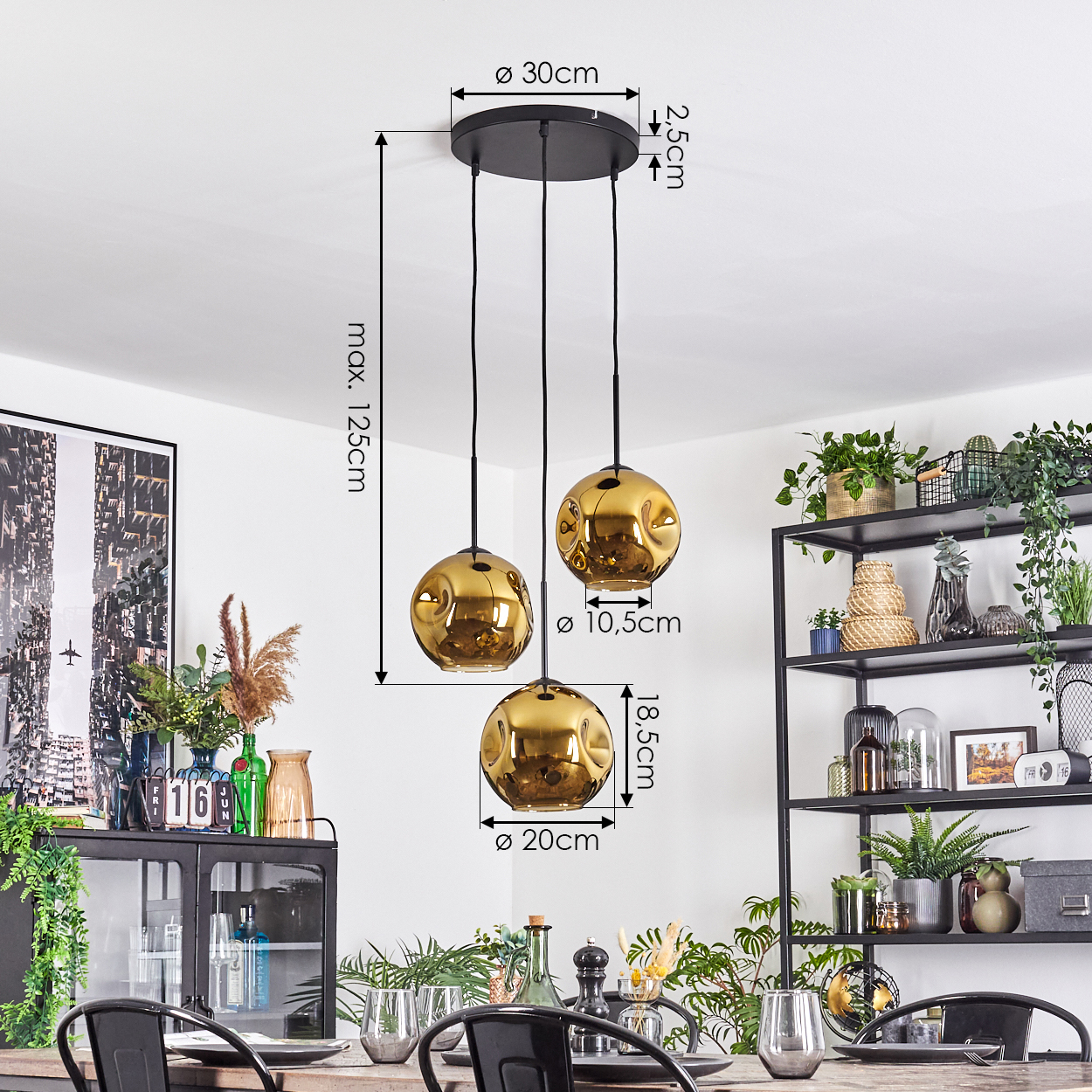 Drei goldene Pendelleuchten hängen über einem Esstisch. Rechts ein schwarzes Regal mit Pflanzen. Links ein Schrank mit Dekoration.