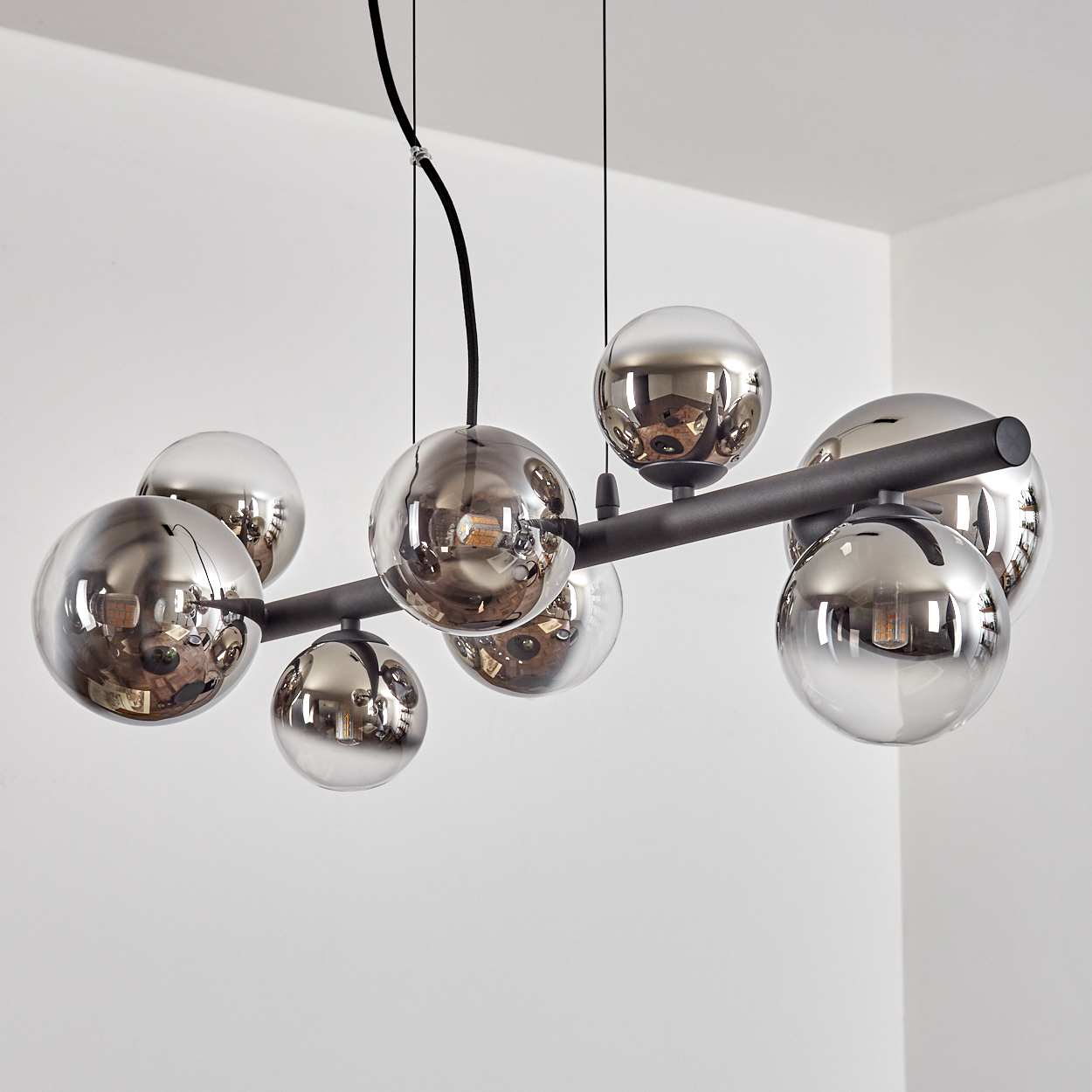 Eine moderne Deckenleuchte mit mehreren reflektierenden, kugelförmigen Lichtern. Sie hängt von der Decke vor einer weißen Wand.