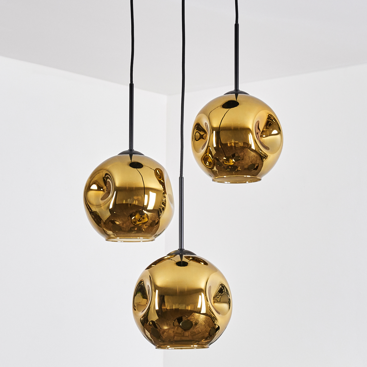 Drei goldene, strukturierte, kugelförmige Pendelleuchten hängen vor einer weißen Wand und Decke. Schwarze Kabel und Armaturen sind sichtbar.