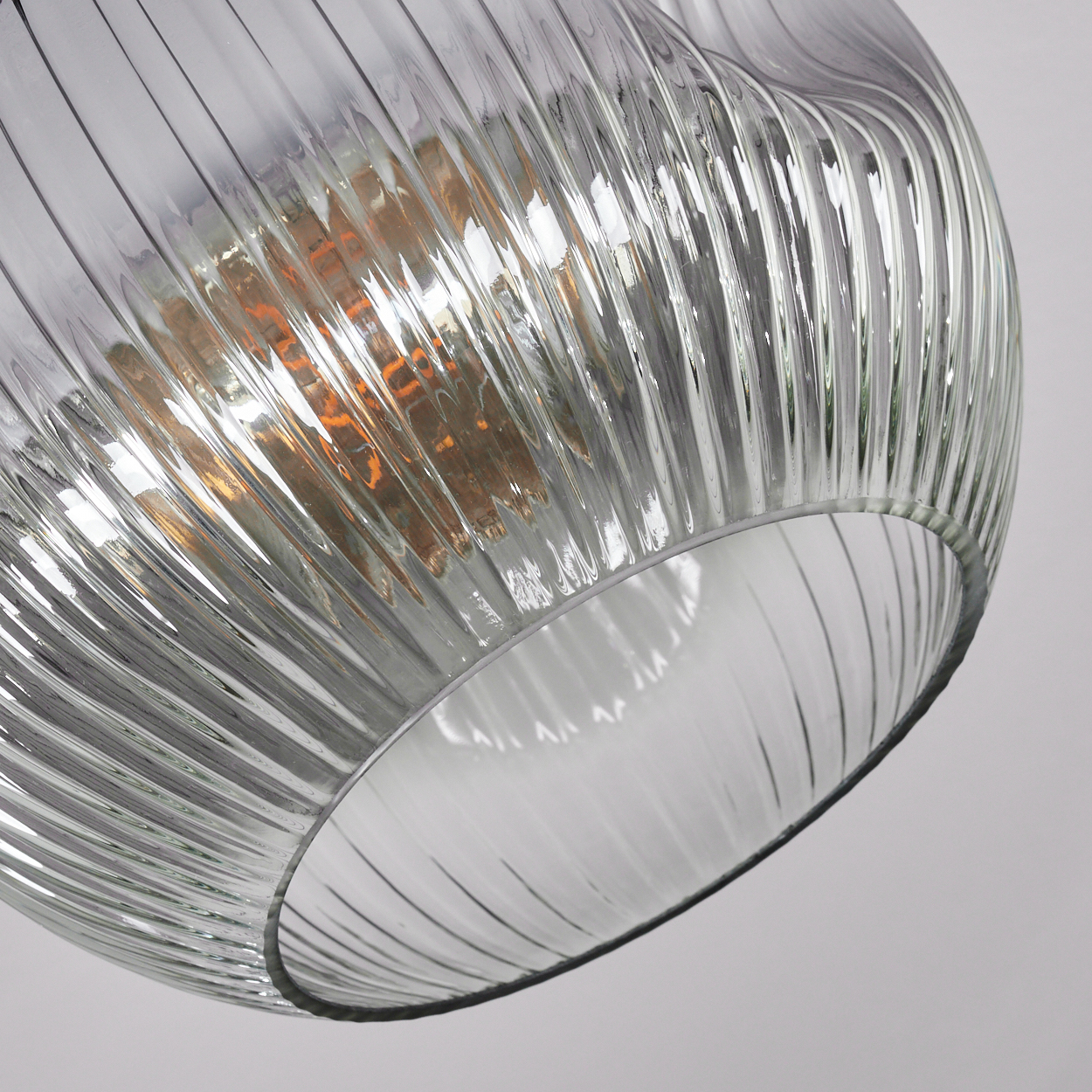 Nahaufnahme eines Lampenschirms aus Glas mit vertikalen Rippen. Im Inneren ist eine orangefarbene Glühbirne zu sehen. Der Hintergrund ist weiß.