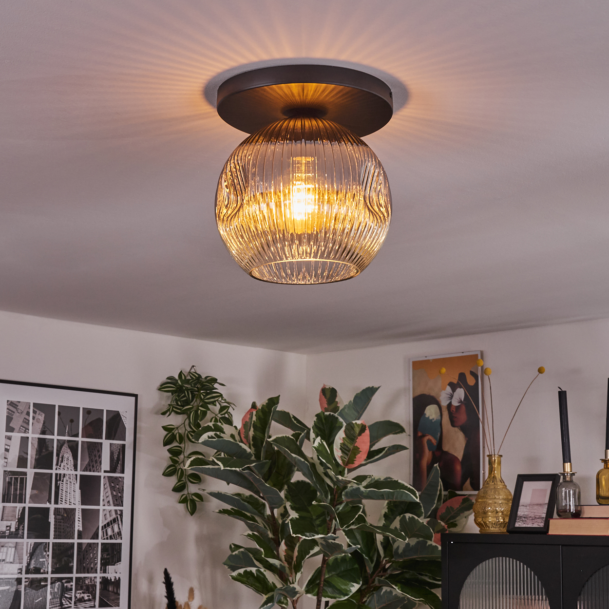 Eine dekorative Deckenlampe mit Glasschirm und warmem Licht, umgeben von Pflanzen und gerahmten Kunstwerken.