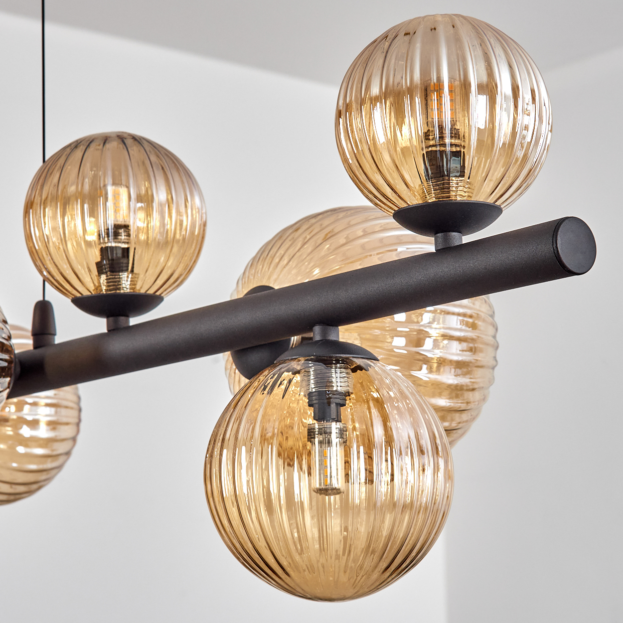 Eine moderne Deckenleuchte mit mehreren bernsteinfarbenen, kugelförmigen Glasschirmen. Sie sind beleuchtet und hängen an einem schwarzen Metallrahmen.