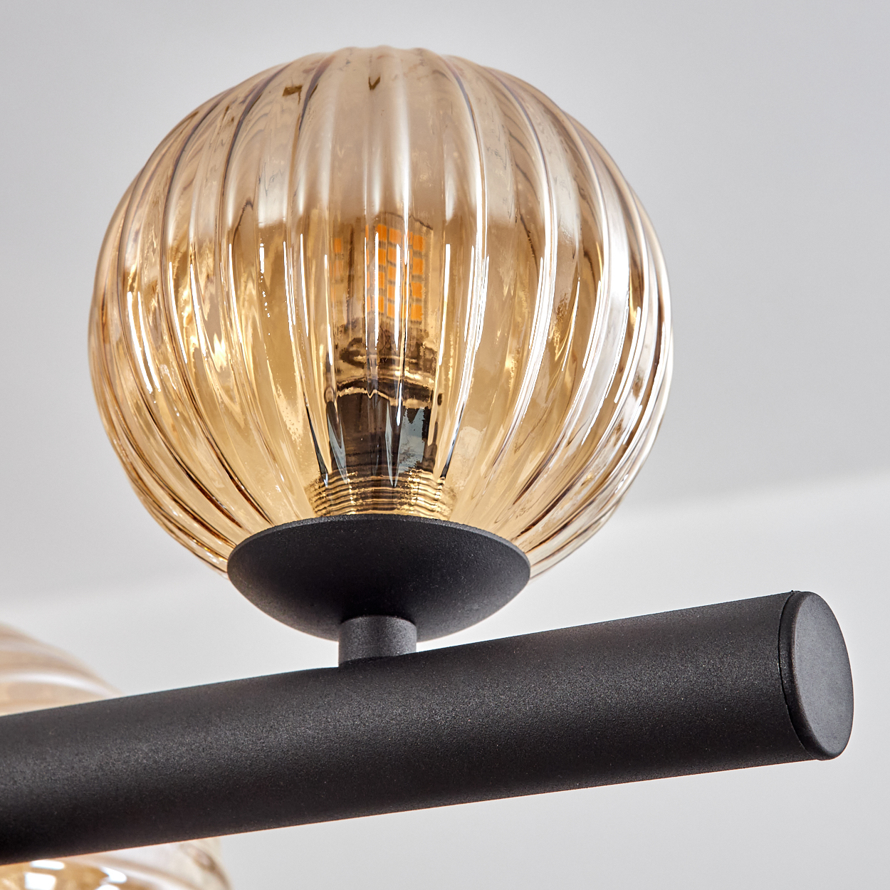 Nahaufnahme einer modernen Leuchte. Sie hat einen runden, bernsteinfarbenen Glasschirm mit gerilltem Design, schwarze Stange.