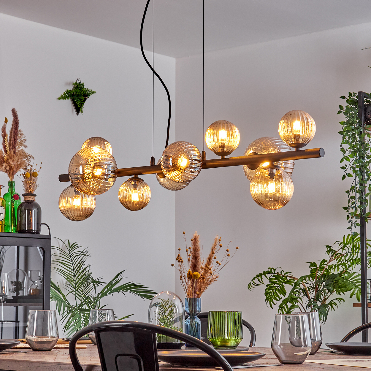 Ein Esszimmer mit Holztisch, modernem Kronleuchter mit Kugellichtern und dekorativen Pflanzen. Die Umgebung ist hell und einladend.