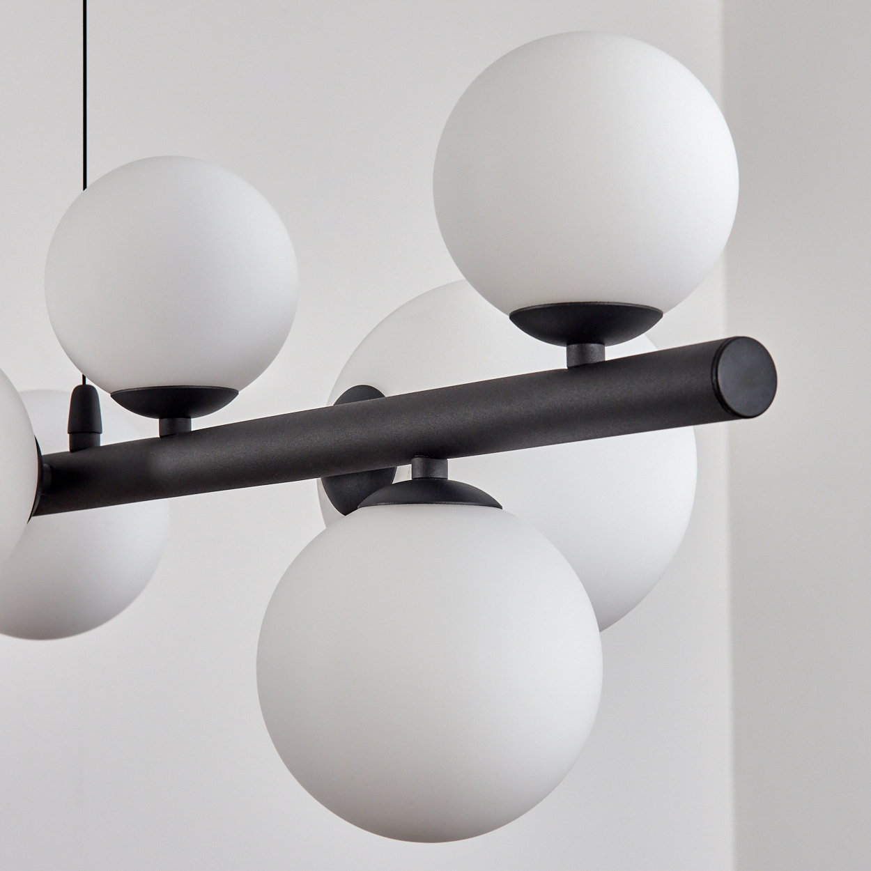 Eine moderne Hängeleuchte mit weißen Kugeln und einem schwarzen Rahmen. Der Hintergrund ist eine schlichte weiße Wand.